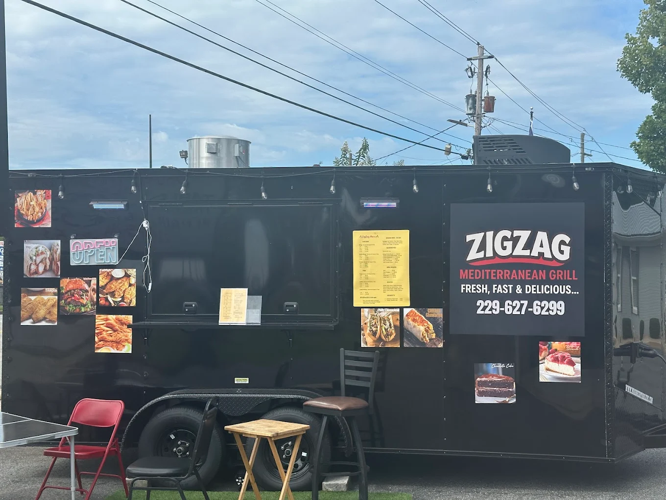 Black food truck with "Zigzag Mediterranean Grill" signage, menu photos, and outdoor seating area.