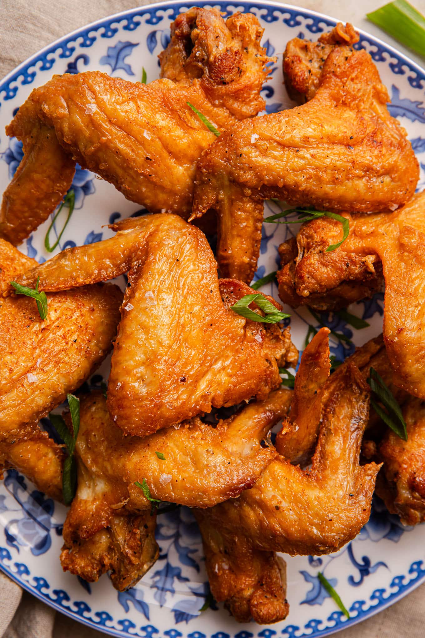 Crispy fried chicken wings on decorative blue and white plate with green onion garnish.